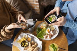 Two people holding phones and taking pictures of food on the table